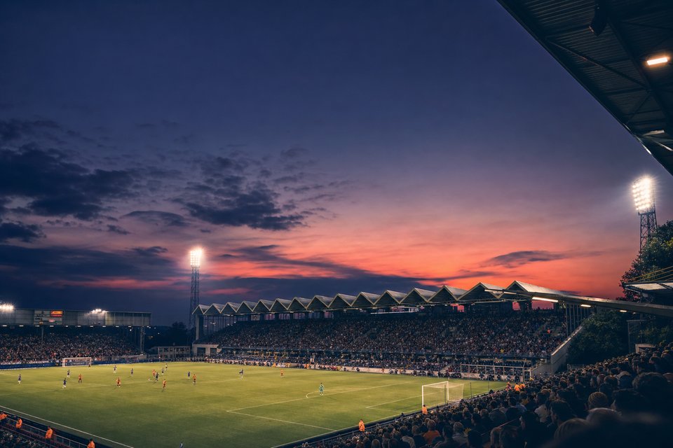 Belgisch voetbalstadion bij zonsondergang met verlichte lichtmasten