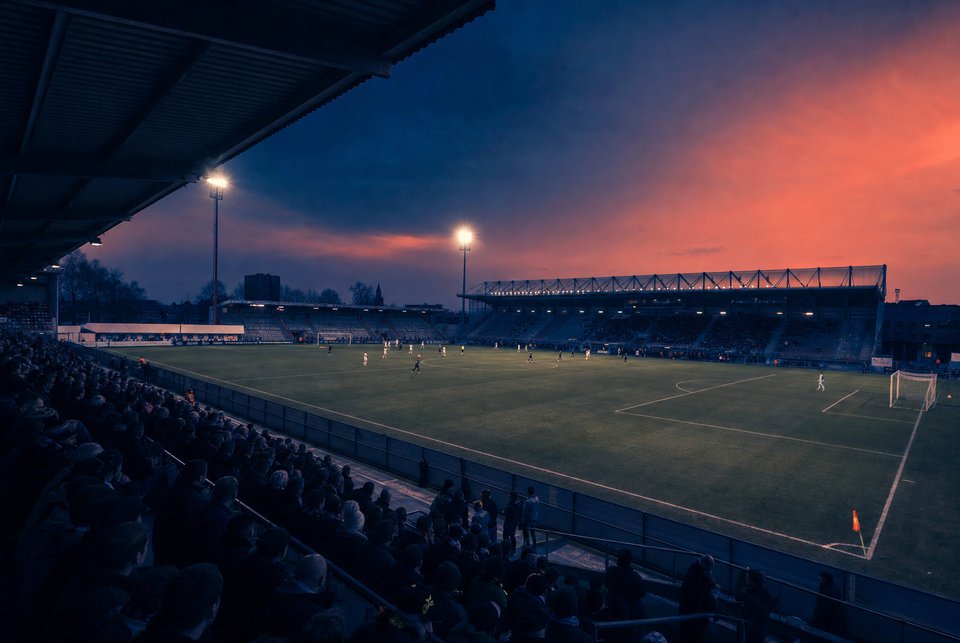 Belgisch voetbalstadion vanaf een steile tribunehoek in de schemering