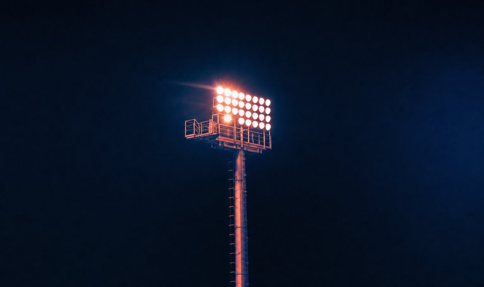Eén lichtmast met brandende lampen tegen een zwarte nachtlucht