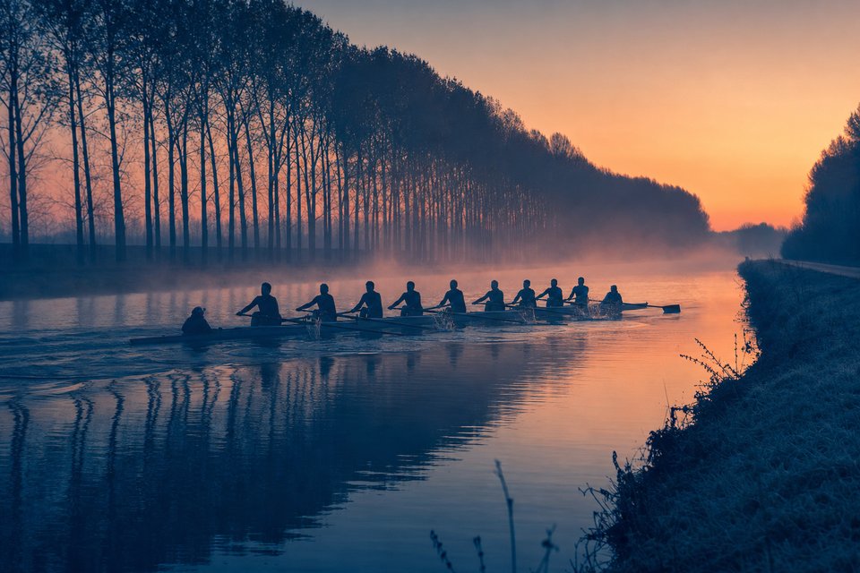 Roeiachten op een kanaal bij zonsopkomst met mist over het water
