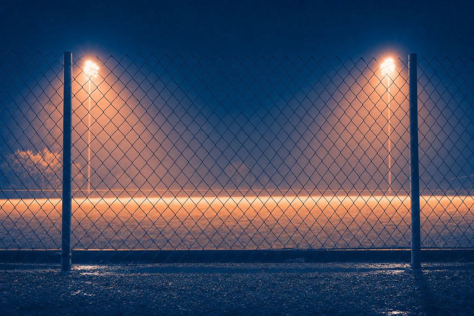 Verlicht voetbalveld bij nacht gezien door een harmonicagaas