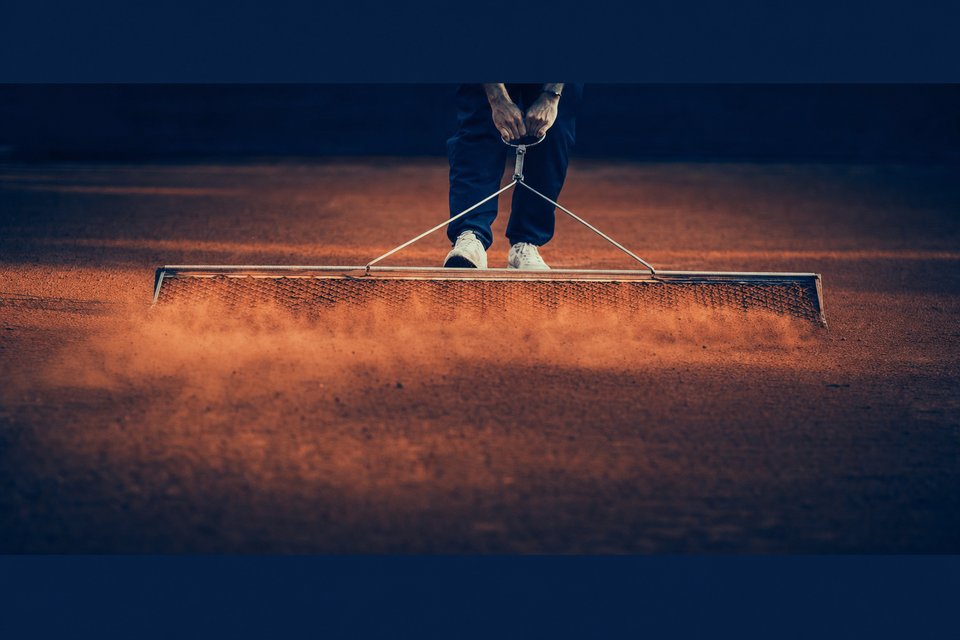 Gravelbaan die met een sleepnet wordt geveegd, okergeel stof in laag licht