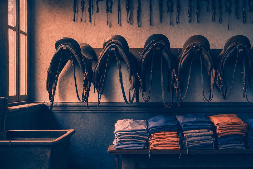 Zadelkamer met renzadels op een rek en opgevouwen kleuren in effen vlakken