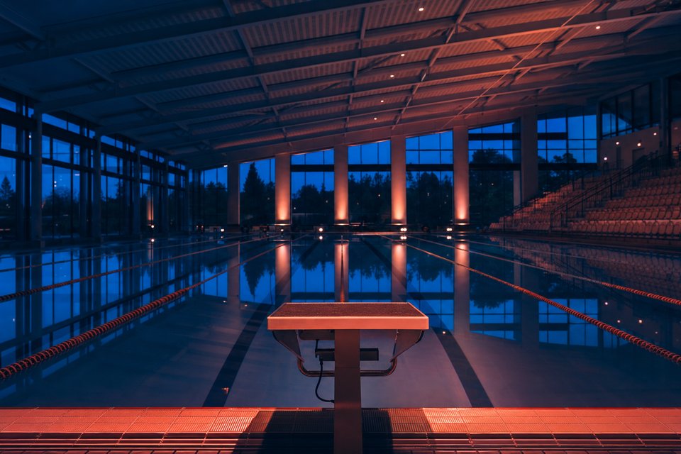 Overdekt wedstrijdbad in het blauwe uur met gespannen baanlijnen