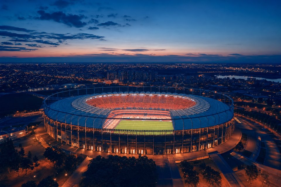 Voetbalstadion van bovenaf in de schemering met oplichtende lichtmasten