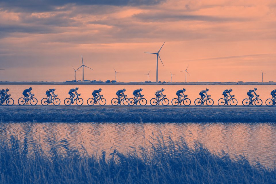 Wielerpeloton op een dijkweg in het polderlandschap met windturbines